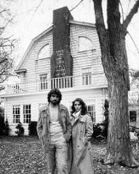 Image shows actors who played George and Kathy Lutz standing behind the Amityville house.